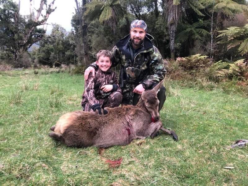 A man and his son pose with a dead deer.