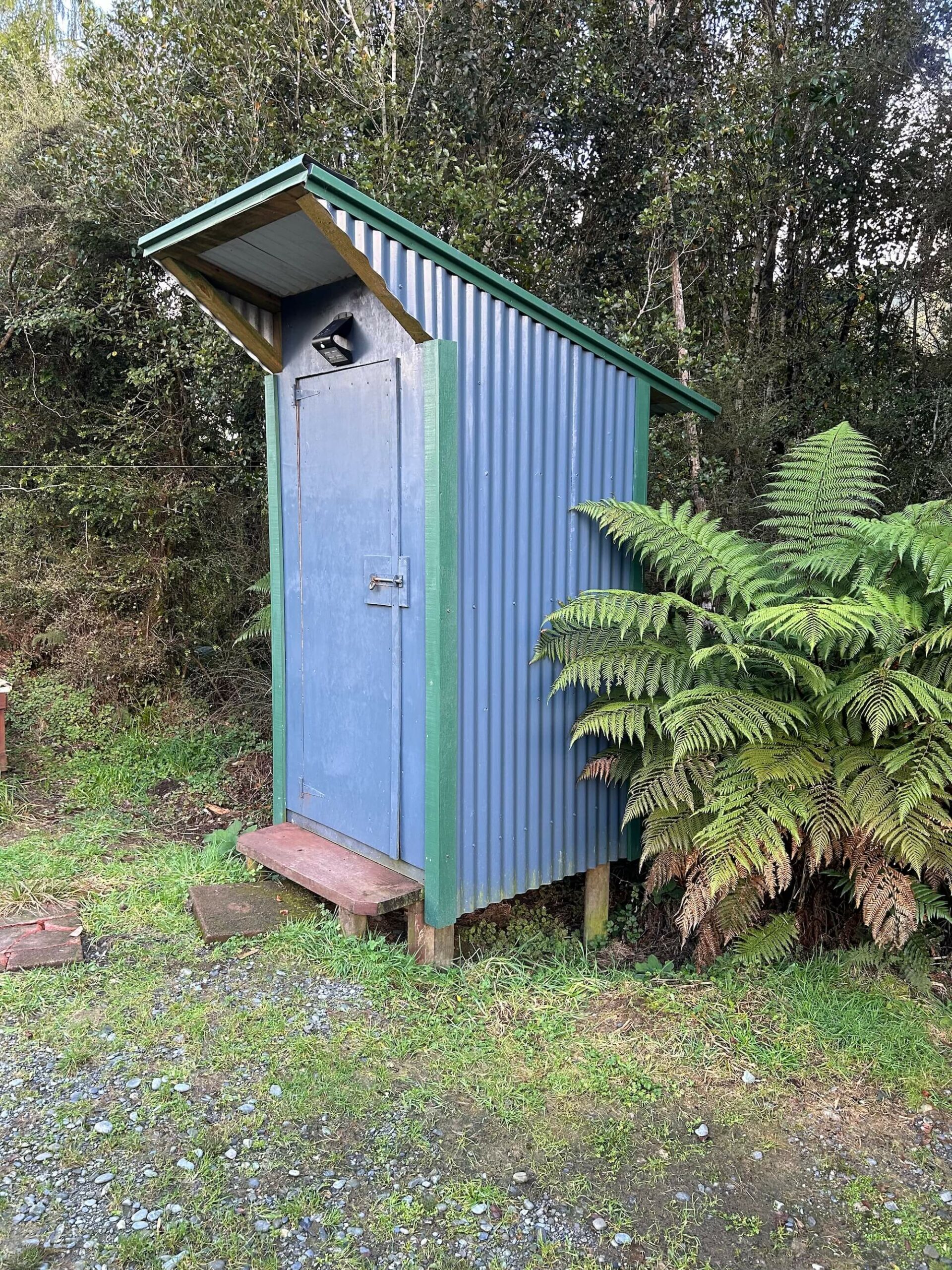 An outhouse with a blue roof in the woods.